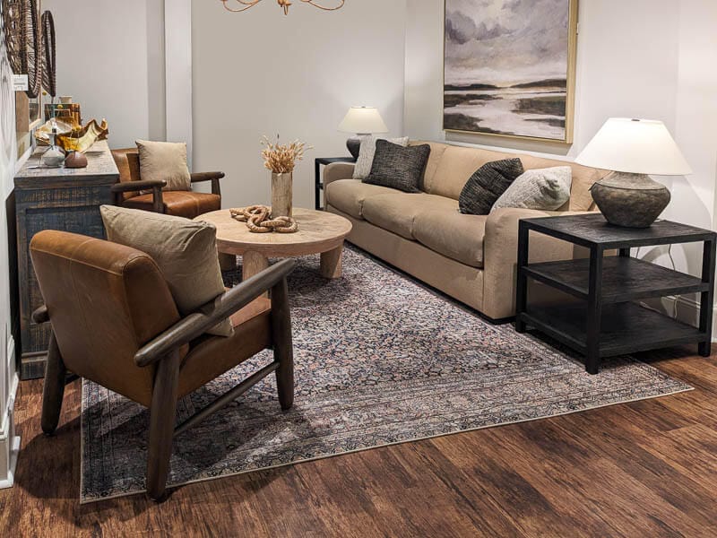 Livingroom display with gray sofa, leather cushions with wooden arm chairs and round cream colored coffee table